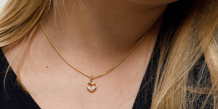 Goldene Halskette mit Herzanhänger und Zirkonia am Dekolleté getragen