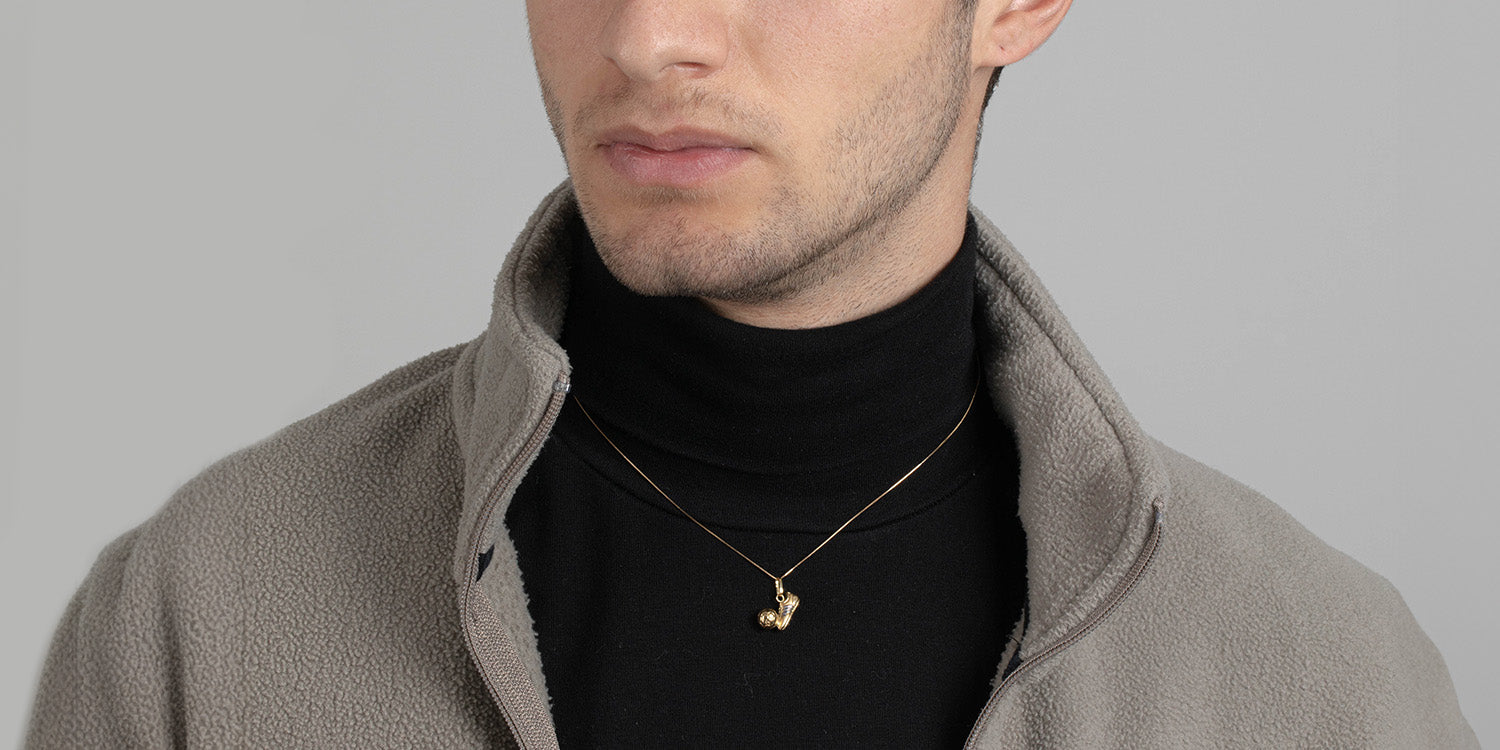 Mann trägt eine dünne goldene Halskette mit Fußball-Anhänger, gekleidet in schwarzem Rollkragenpullover und grauer Jacke